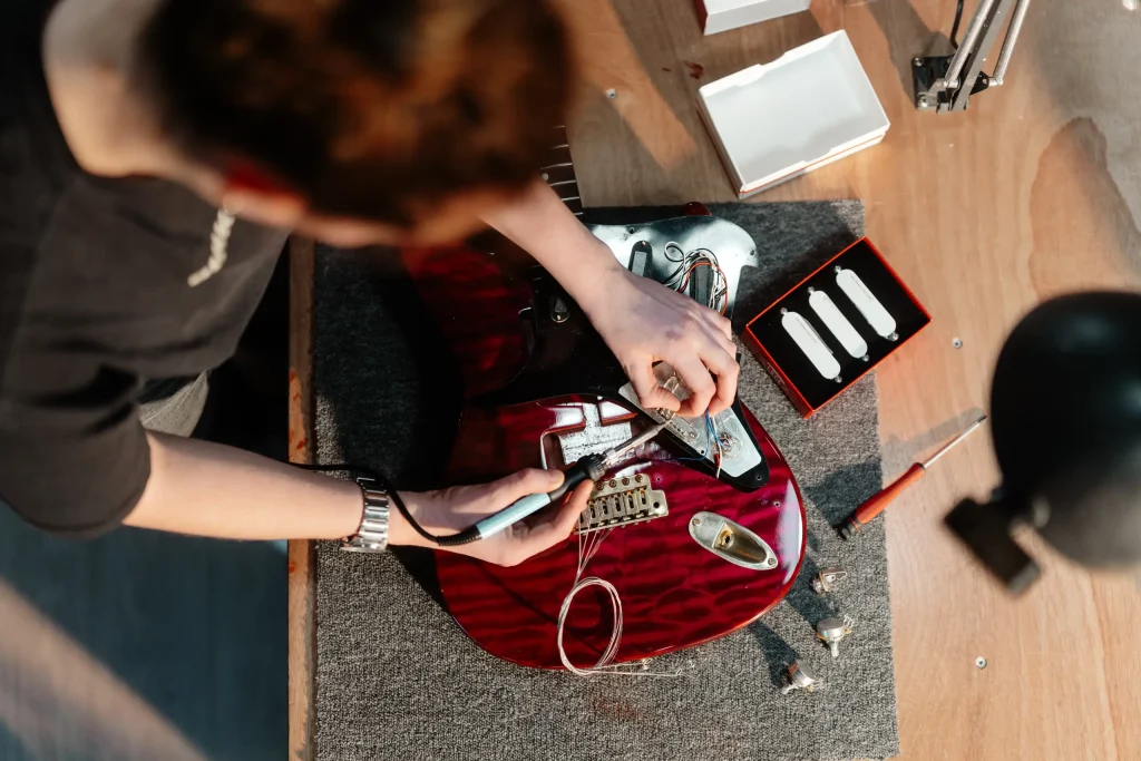 Luthier câblant les micros d'une guitare électrique rouge, vue de dessus