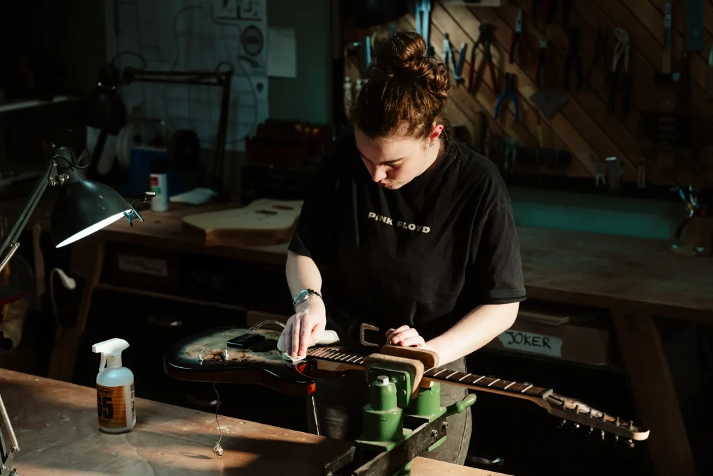 Luthier effectuant la réfection des frettes d'une guitare électrique dans son atelier