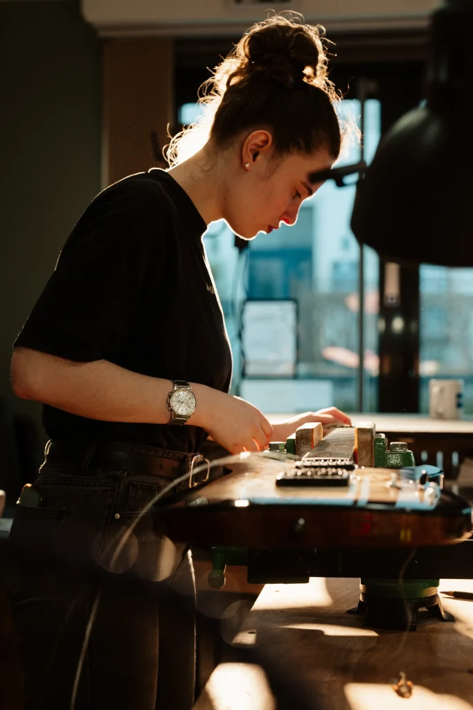 Luthière posant les frettes sur le manche d'une guitare électrique dans son atelier